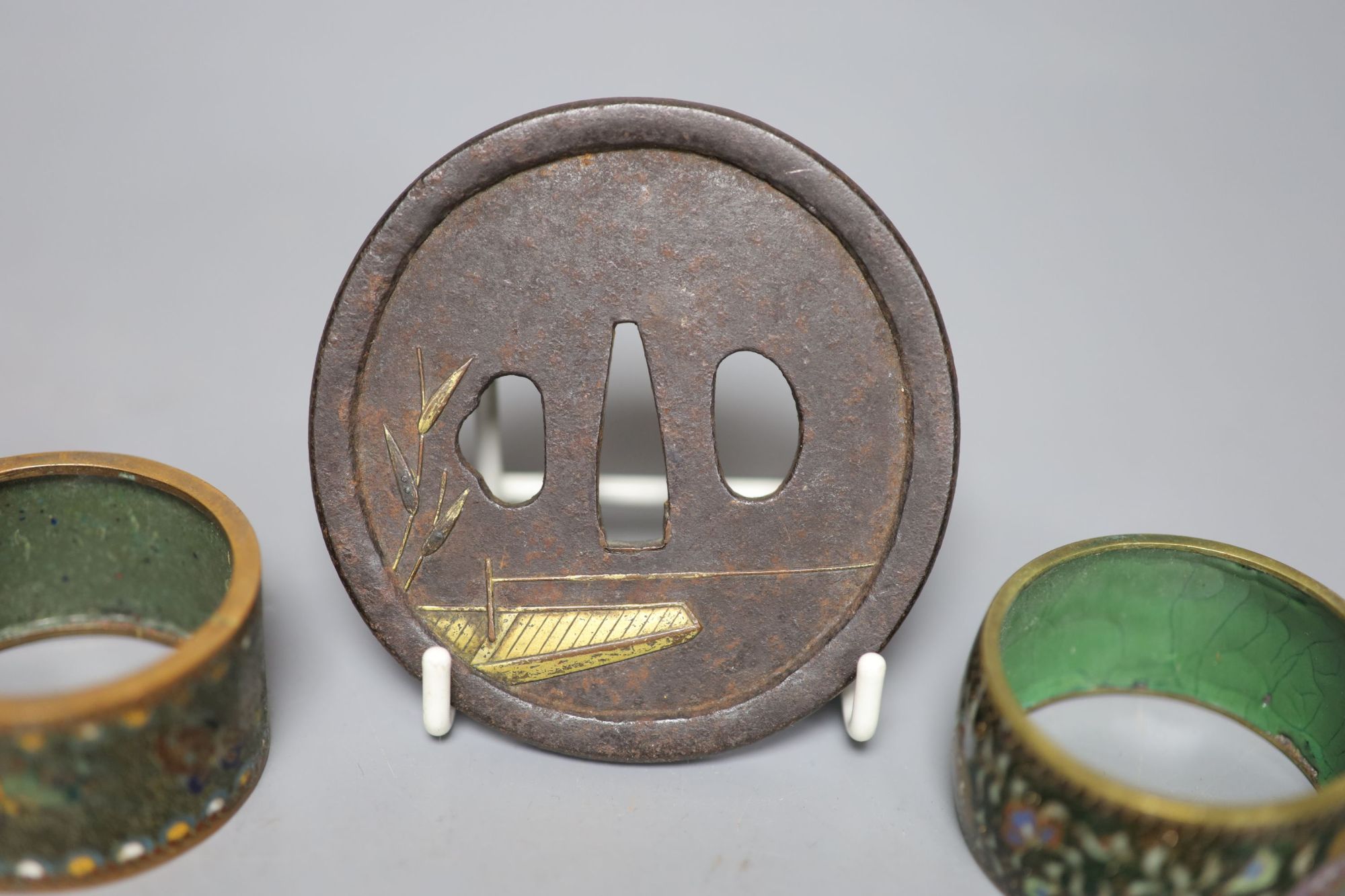 A 19th century Japanese iron and parcel gilt tsuba, unsigned, 8cm and two cloisonne enamel napkin rings.